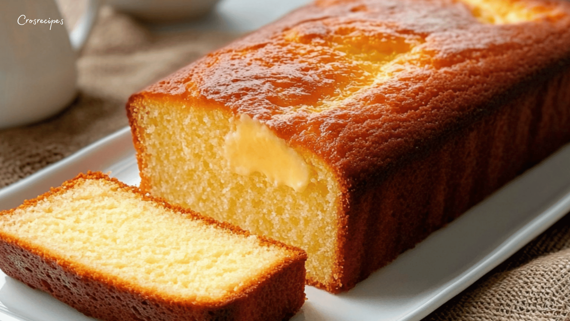 Gâteau au yaourt extra moelleux, doré et tranché, accompagné d’une tasse de thé et d’une nappe en coton blanc.