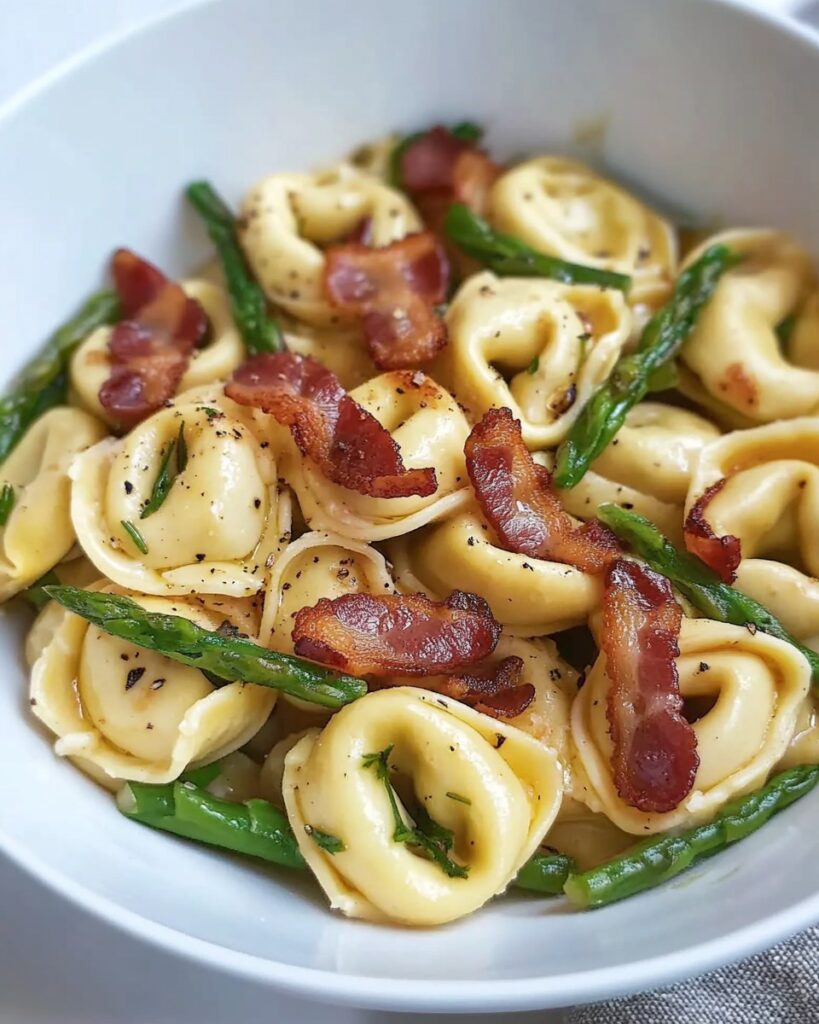 Assiette de tortellini avec asperges, bacon croustillant et beurre noisette, garnie de parmesan râpé et de feuilles de basilic frais.