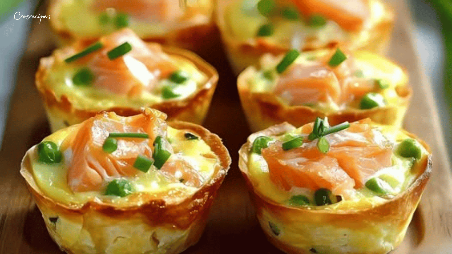 Mini quiches dorées aux poireaux et saumon fumé, servies sur une assiette avec des brins de ciboulette.