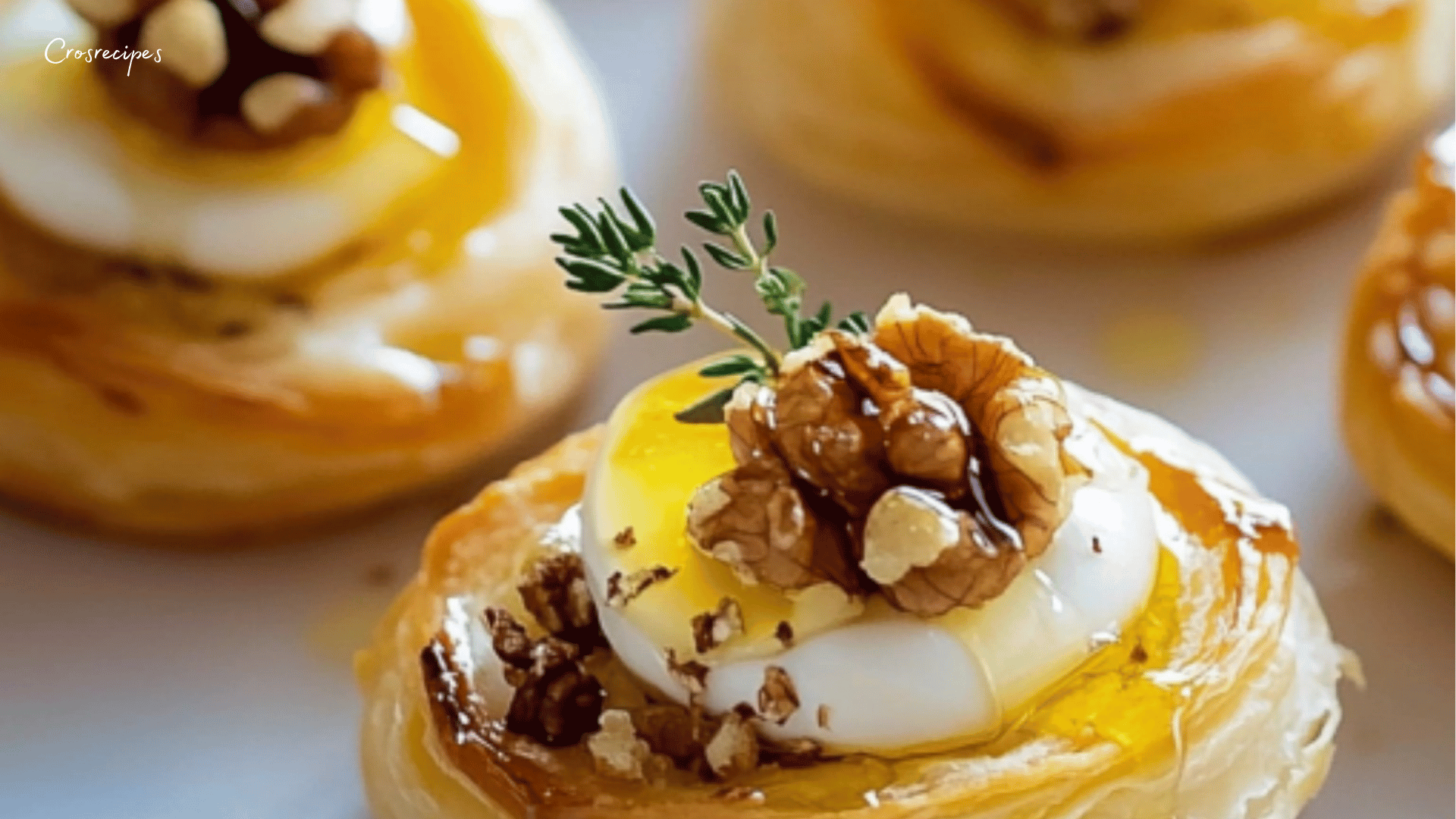 Bouchées feuilletées dorées avec fromage frais, cerneaux de noix et filet de miel sur une assiette élégante.