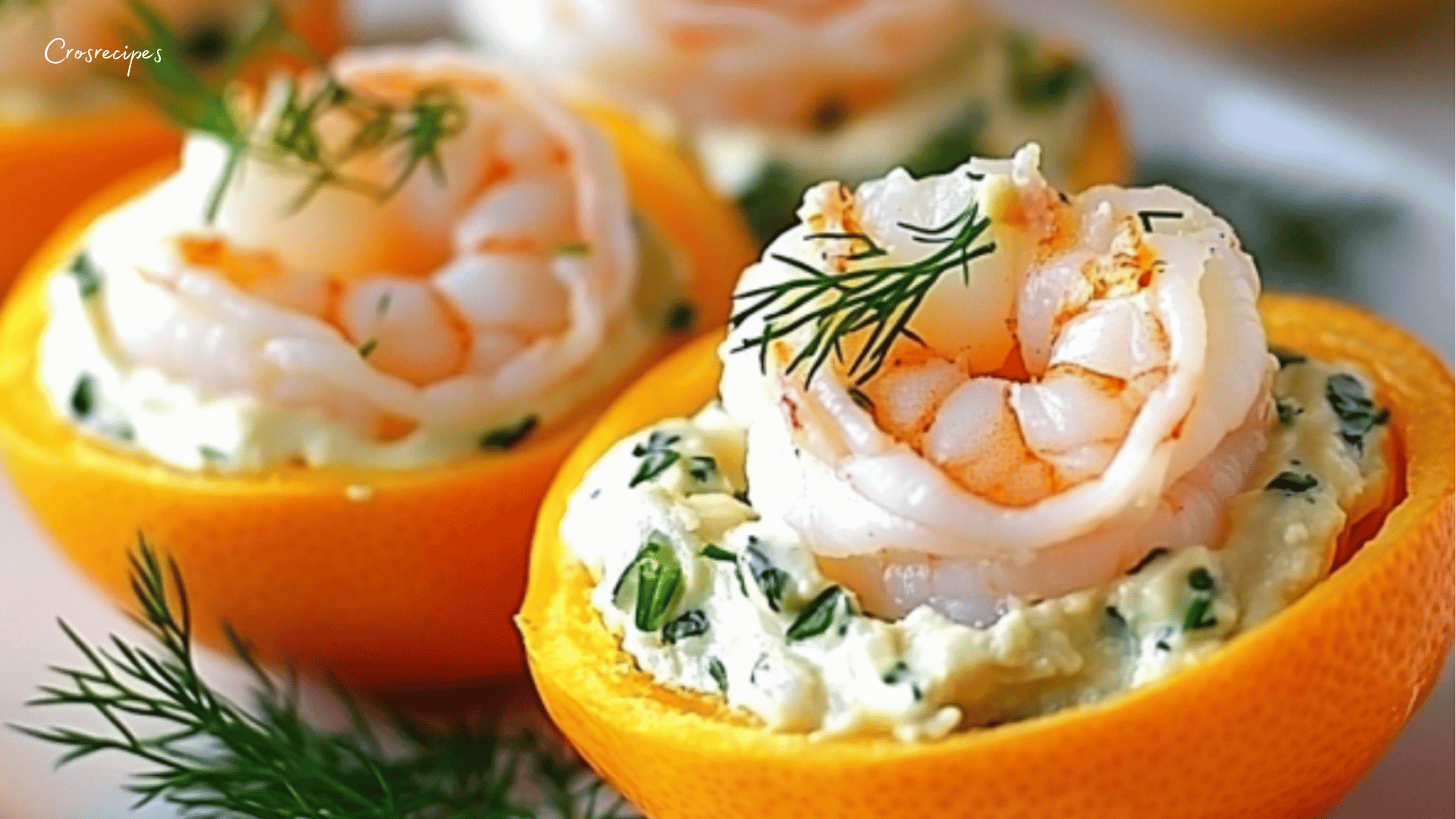 Clémentines farcies aux crevettes avec garniture crémeuse et décoration de baies roses sur une assiette élégante.