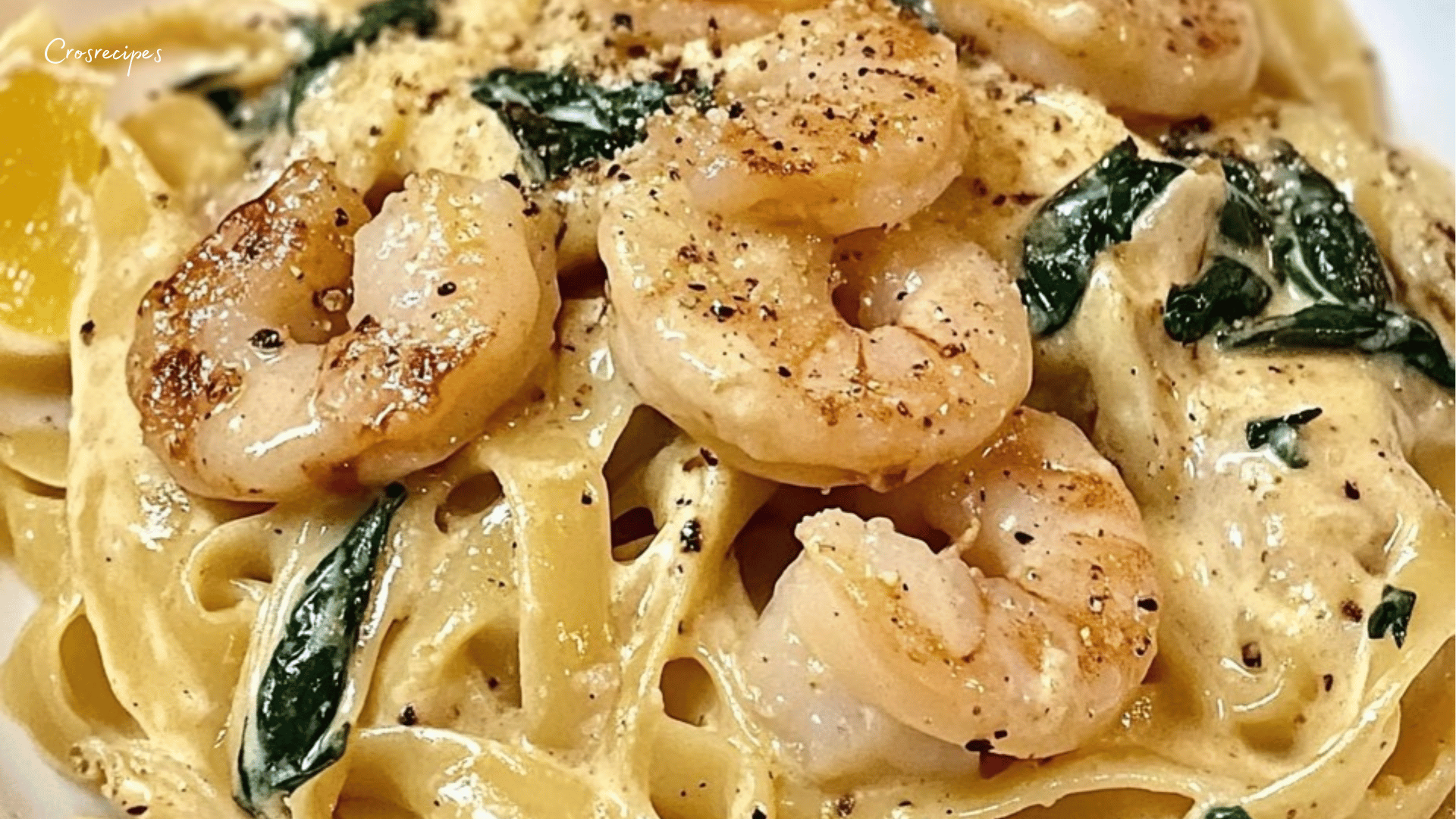 Assiette de tagliatelles crémeuses aux crevettes et épinards, saupoudrée de fromage râpé.