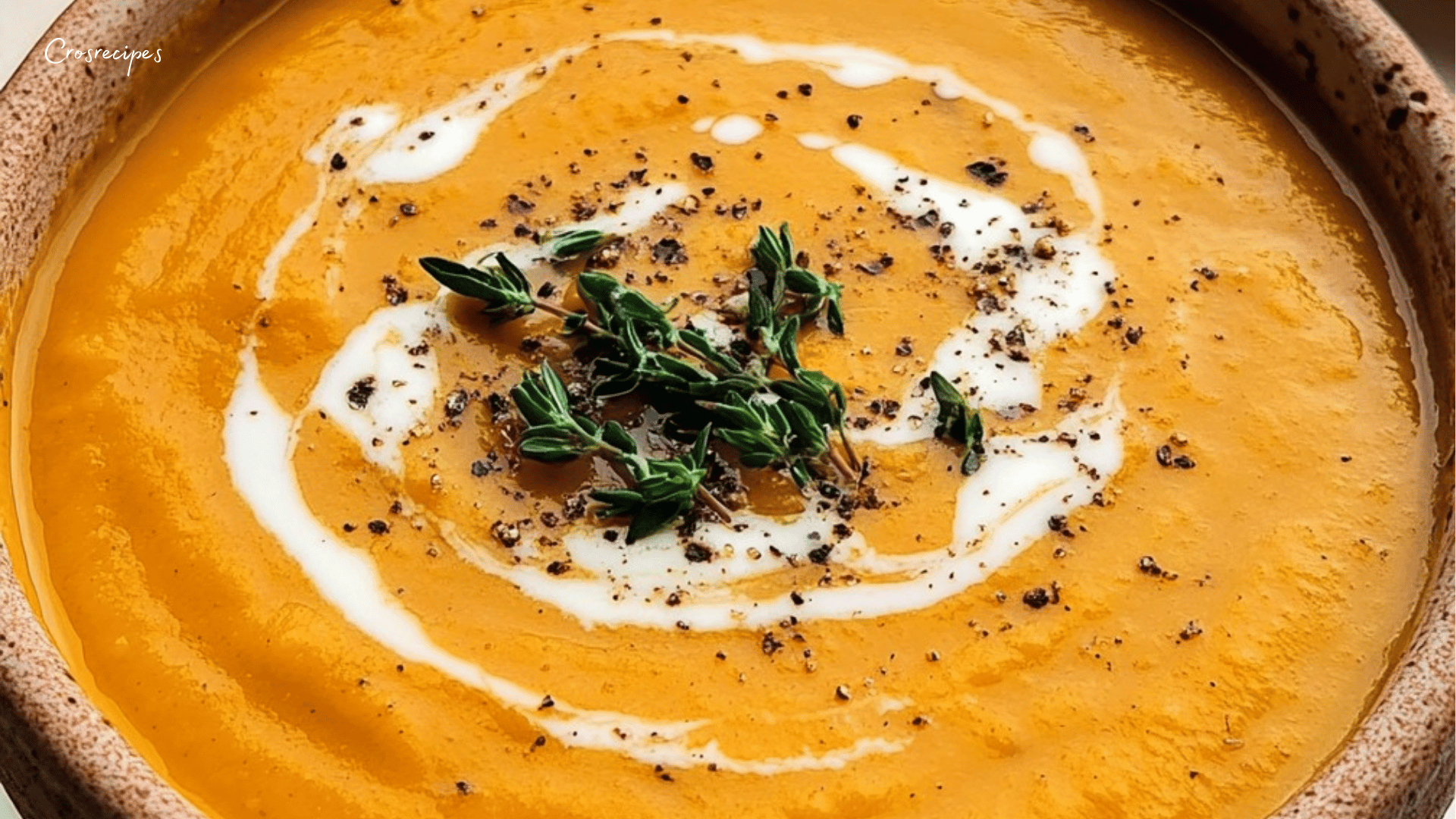 Bol de velouté de potiron doré avec une cuillère de crème fraîche et des graines de courge sur le dessus.