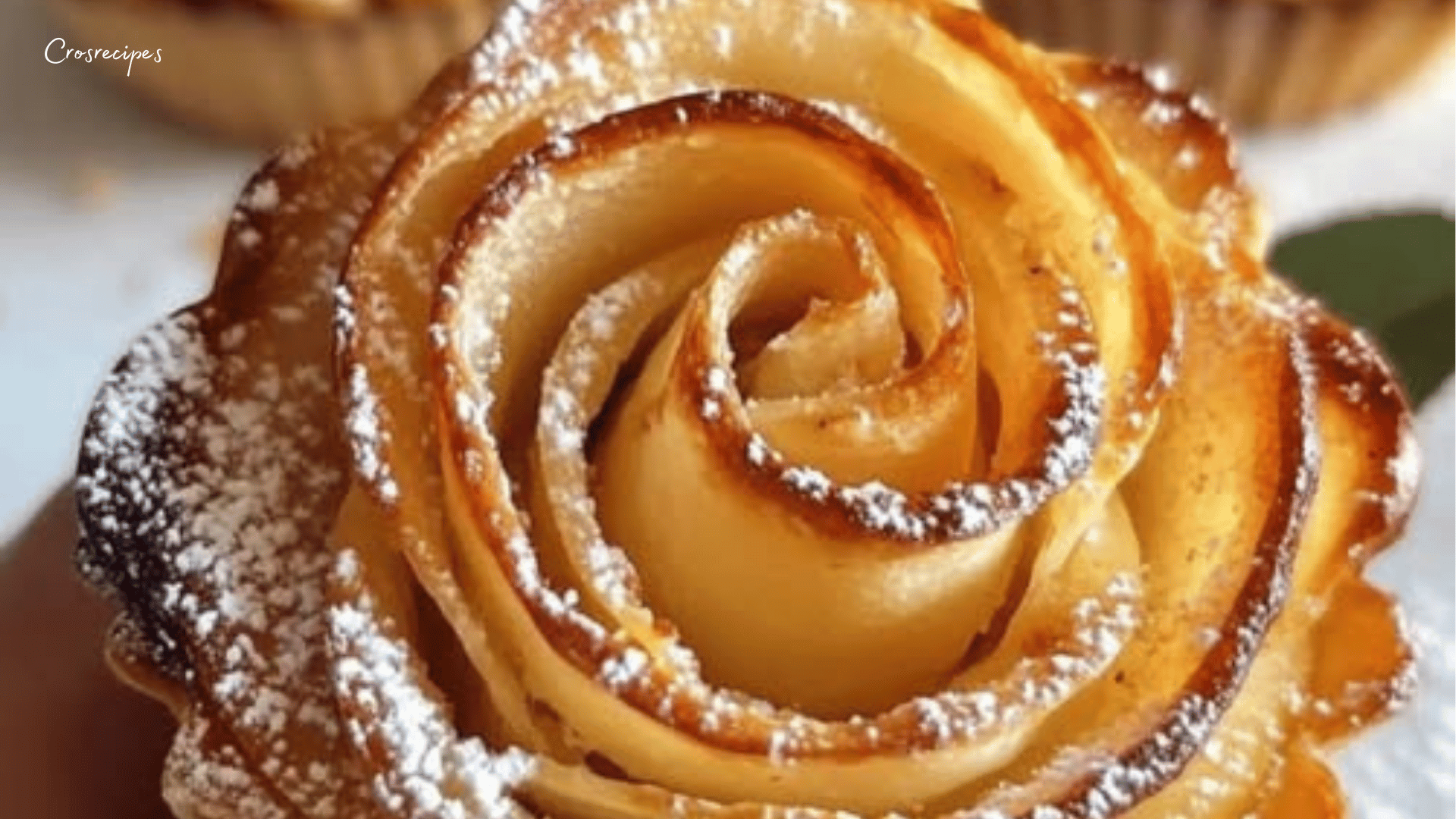 Roses feuilletées aux pommes dorées et saupoudrées de sucre glace, servies dans une assiette élégante.