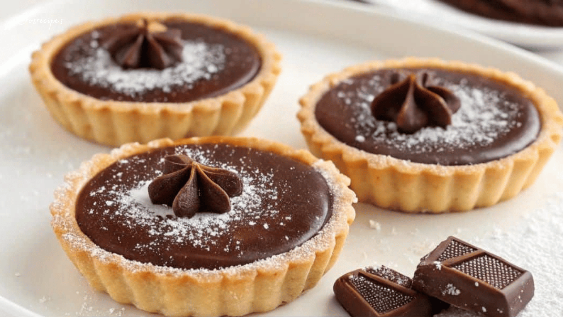 Tartelettes au chocolat avec une garniture crémeuse, servies avec des copeaux de chocolat et une touche de crème fraîche.