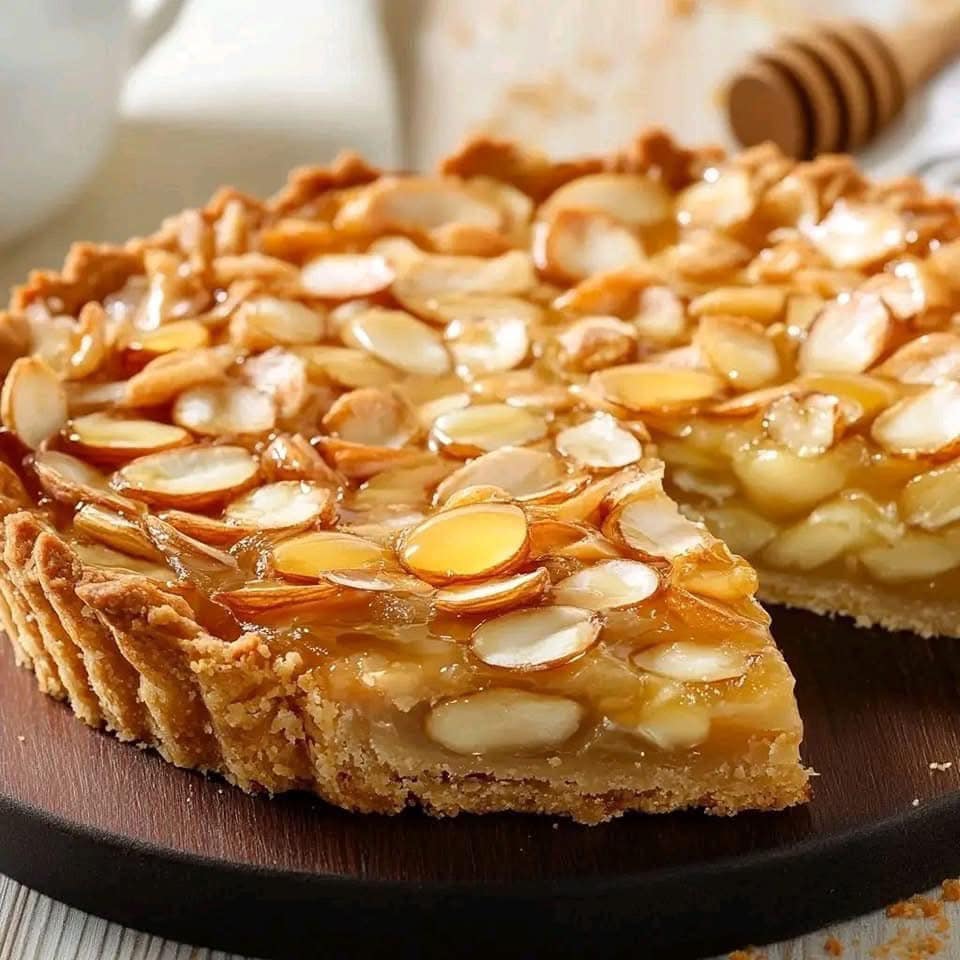 Tarte dorée aux amandes effilées et au miel, avec une pâte sablée croustillante, servie sur une assiette en bois.