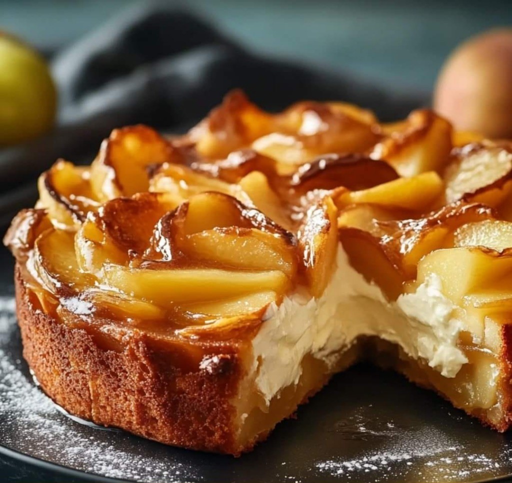 Fondant aux pommes et mascarpone, saupoudré de sucre glace et servi en parts sur une assiette.