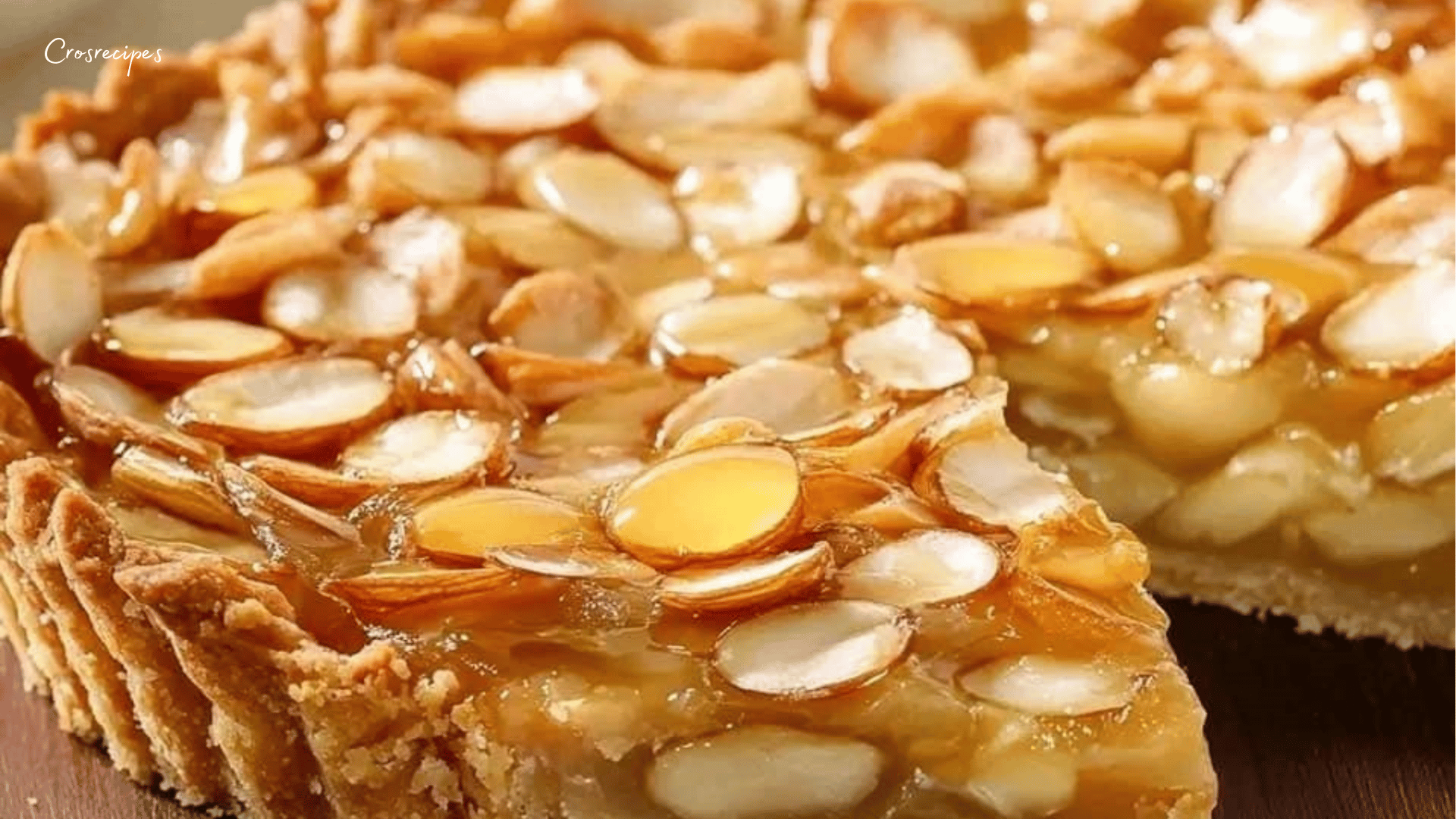 Tarte dorée aux amandes effilées et au miel, avec une pâte sablée croustillante, servie sur une assiette en bois.