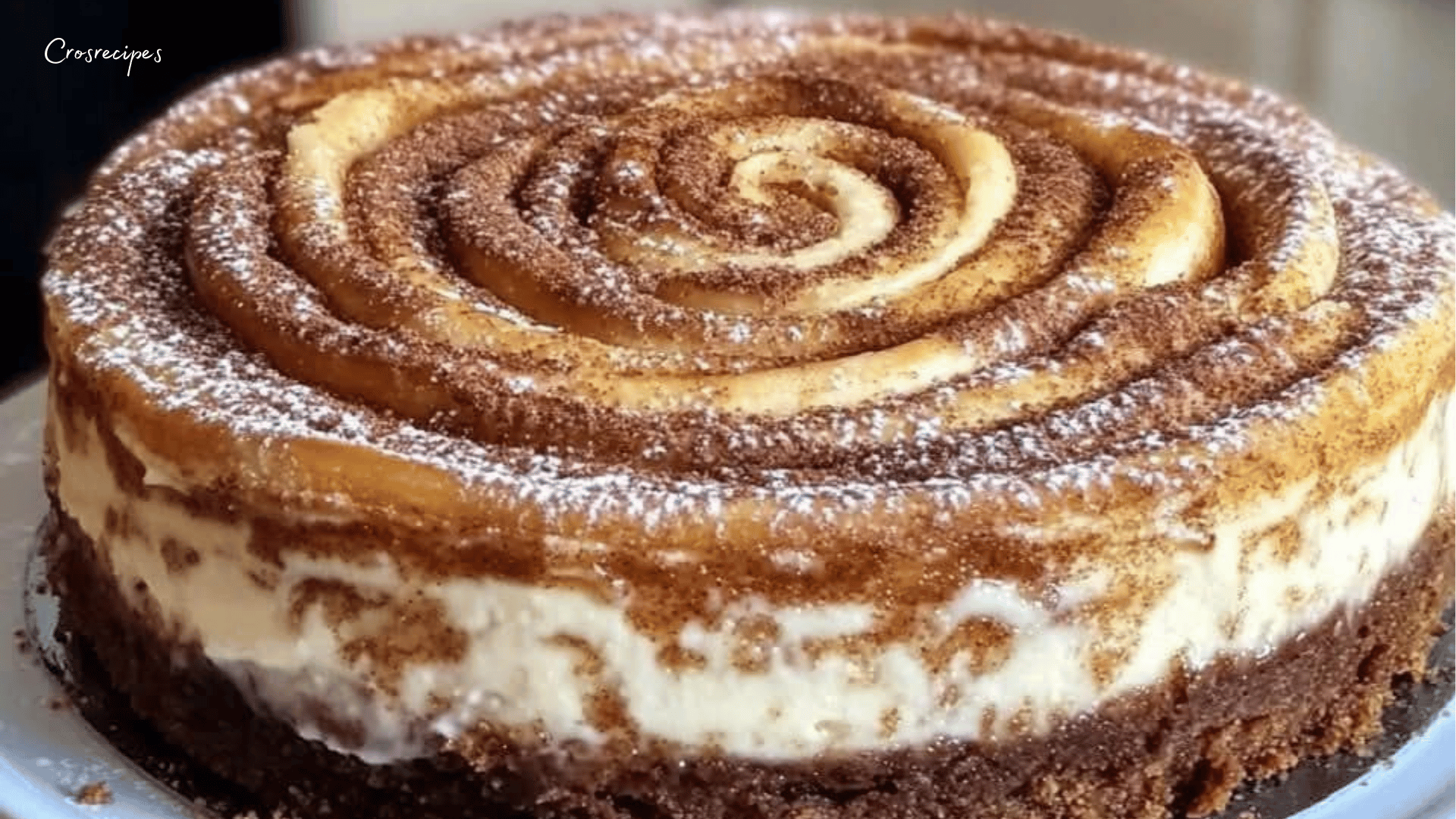 Cheesecake crémeux garni de morceaux de roulés à la cannelle dorés, nappé d’un sirop de miel brillant, servi sur une assiette.