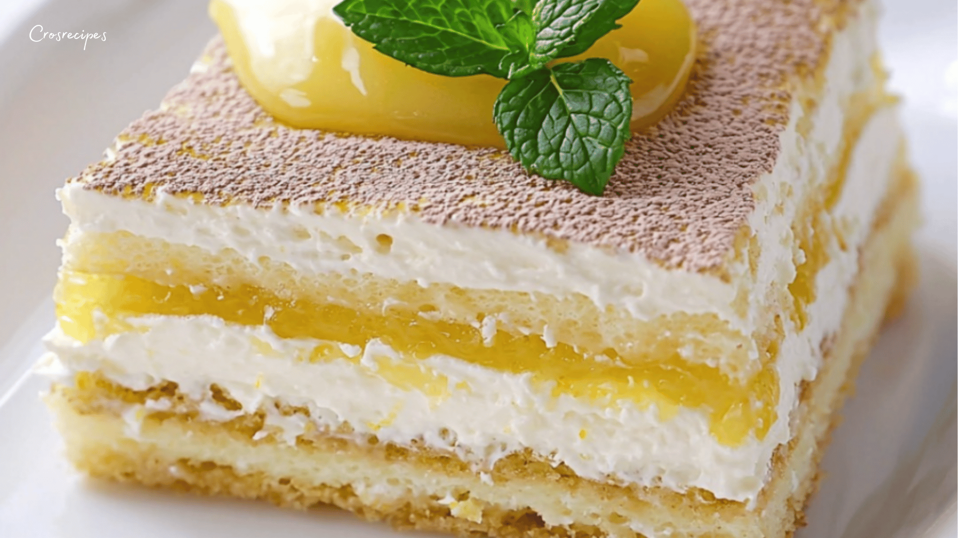 Tiramisu au citron servi dans une verrine, avec des zestes de citron et des feuilles de menthe en décoration, sur une table ensoleillée.