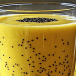 Verre de smoothie kiwi et banane vert onctueux, garni de graines de chia, avec des morceaux de kiwi et de banane en décoration sur une table en bois.