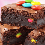 Brownies au chocolat coupés en carrés, avec des M&M’s colorés incrustés et un filet de chocolat blanc en décoration.