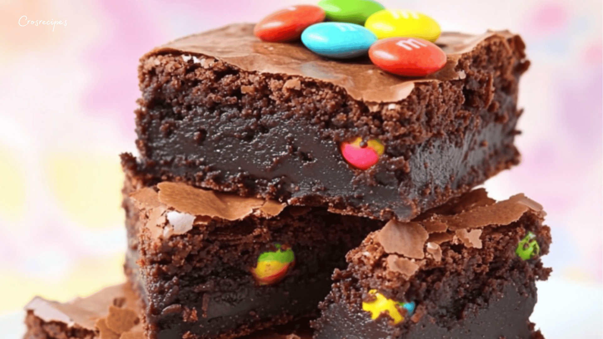 Brownies au chocolat coupés en carrés, avec des M&M’s colorés incrustés et un filet de chocolat blanc en décoration.