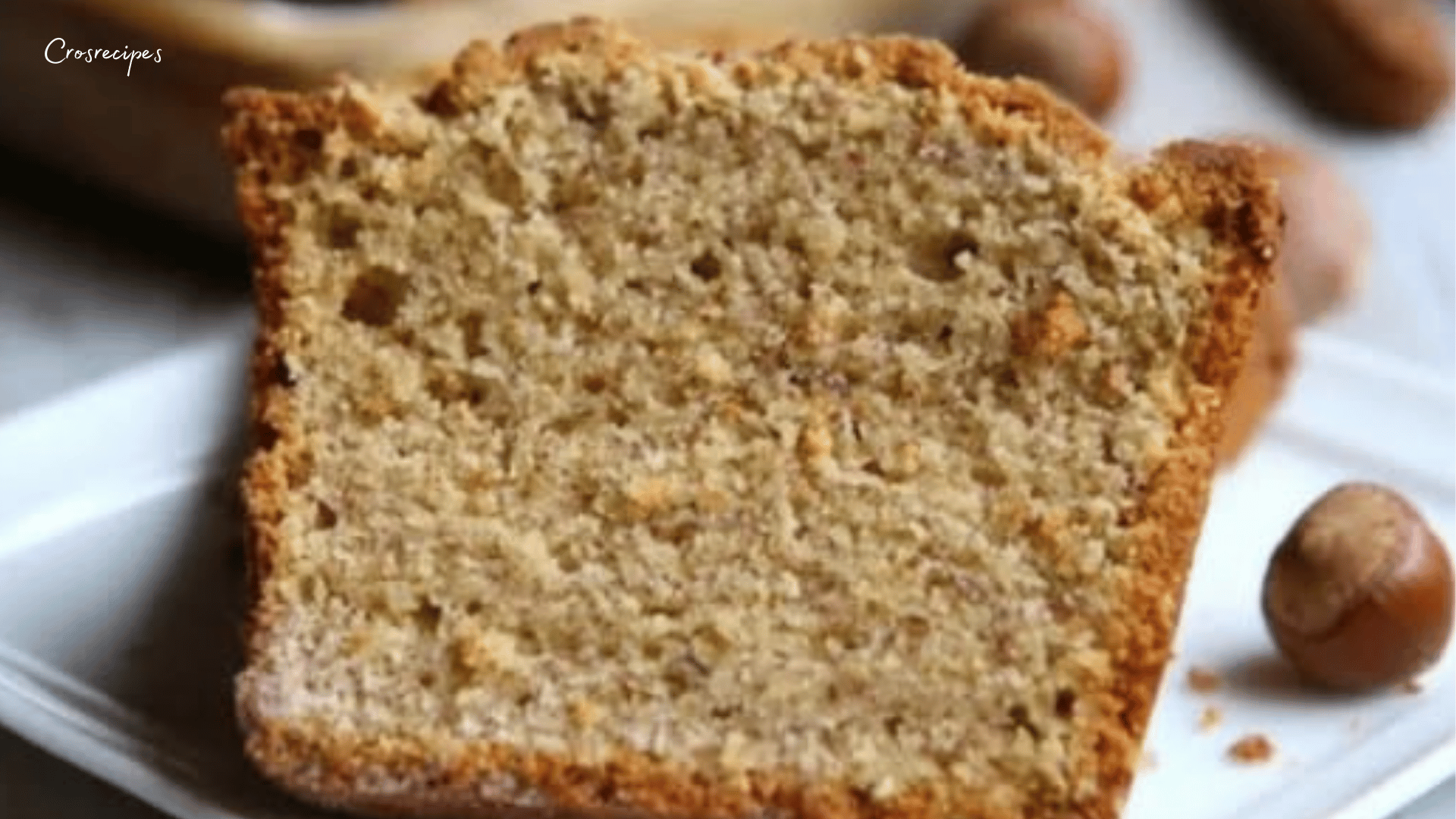 Cake aux noisettes ultra moelleux, doré et fondant, saupoudré de sucre glace, présenté sur une assiette avec une texture aérienne et gourmande.