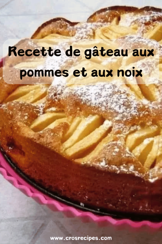 Un gâteau doré aux pommes et aux noix, saupoudré de sucre glace, avec des morceaux de pommes visibles sur le dessus.