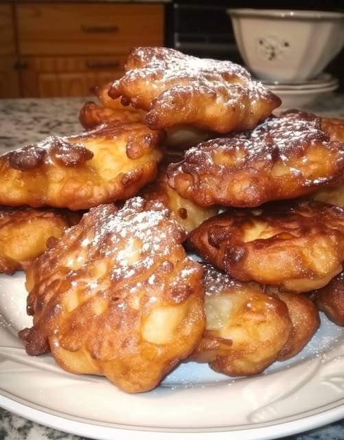 Beignets bretons aux pommes dorés et croustillants, saupoudrés de sucre glace, servis sur une assiette rustique.