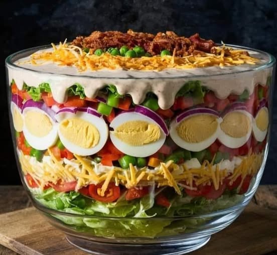 salade à sept étages servie dans un bol transparent avec bacon, œufs, fromage et légumes