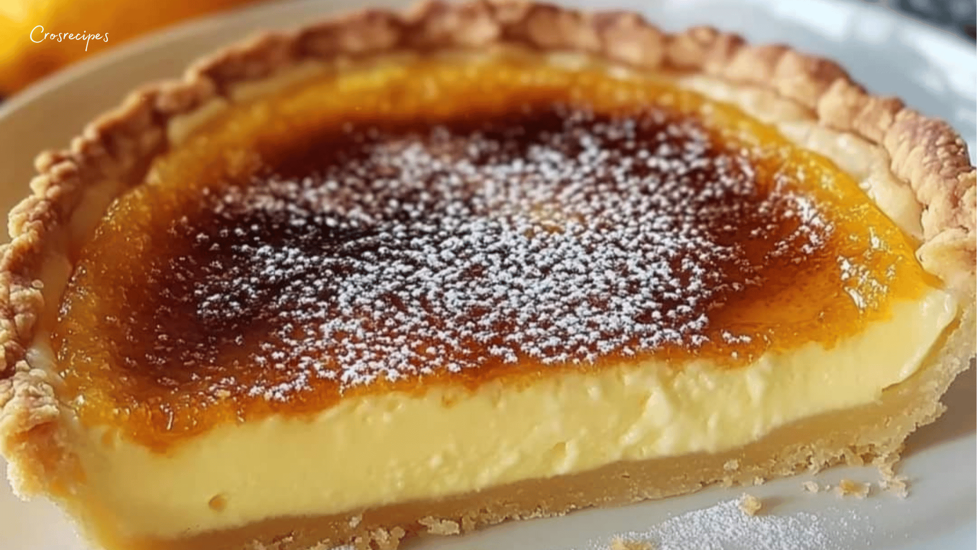 Une tarte façon crème brûlée avec une surface caramélisée dorée et brillante, servie sur une assiette avec des zestes d’orange en décoration.