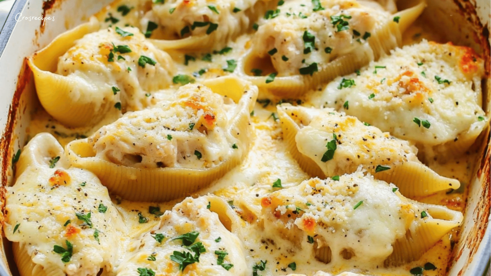 Coquilles farcies au poulet Alfredo gratinées avec du parmesan et du persil frais, servies dans un plat à gratin.