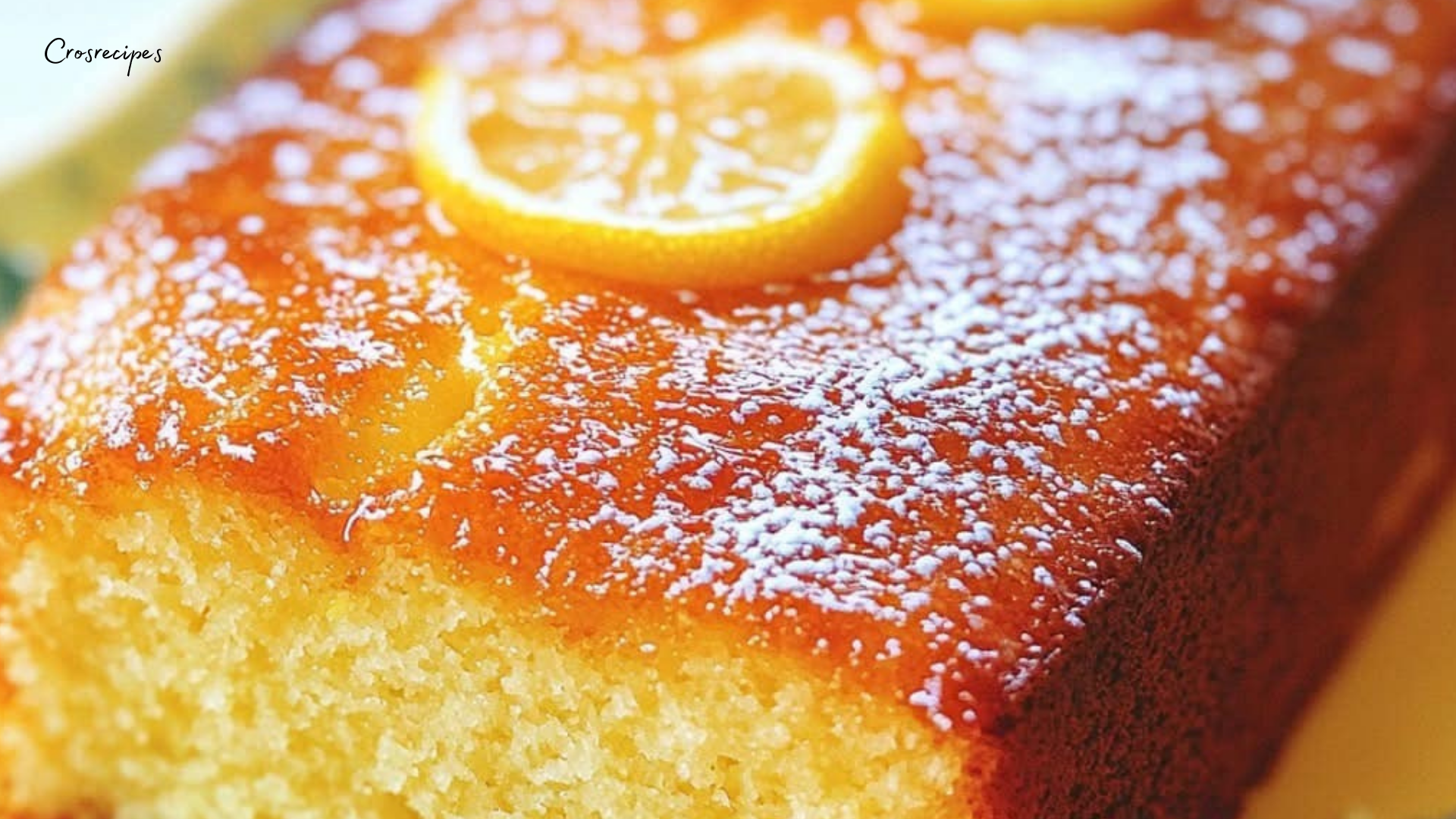 Cake au citron ultra-moelleux avec une croûte dorée et une texture légère, posé sur une assiette avec quelques tranches de citron à côté.