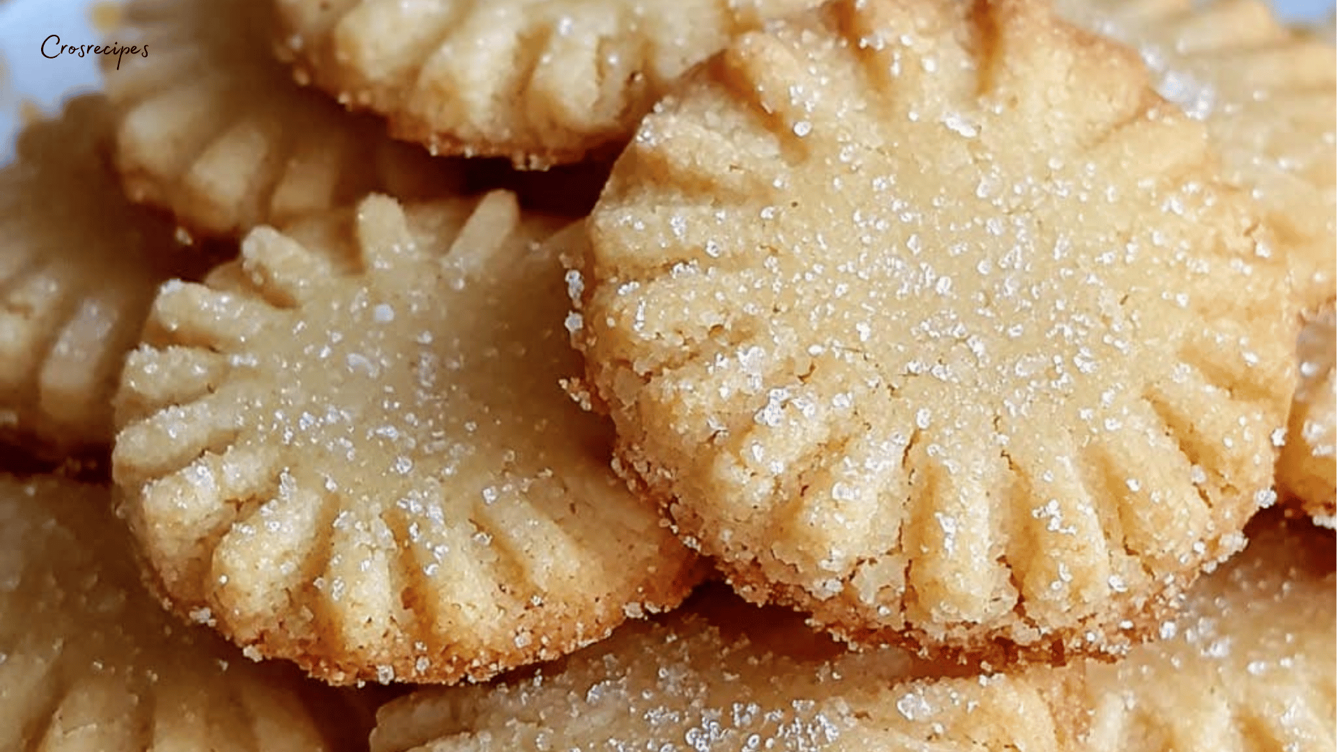 Sablés dorés maison, légèrement saupoudrés de sucre, disposés sur une assiette en porcelaine avec une tasse de thé à côté.