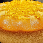 Gâteau moelleux au citron avec glaçage brillant et zestes de citron sur le dessus.