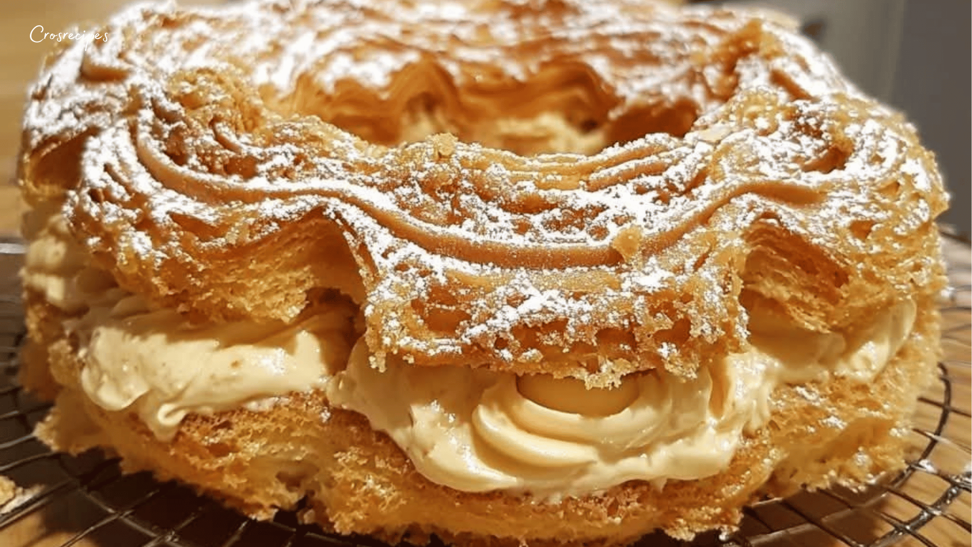 Paris-Brest doré, garni de crème au praliné, saupoudré de sucre glace avec des amandes effilées sur le dessus.