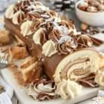 Bûche de Noël roulée au café, saupoudrée de cacao, décorée de grains de café et de sucre glace, sur une planche de bois festive.