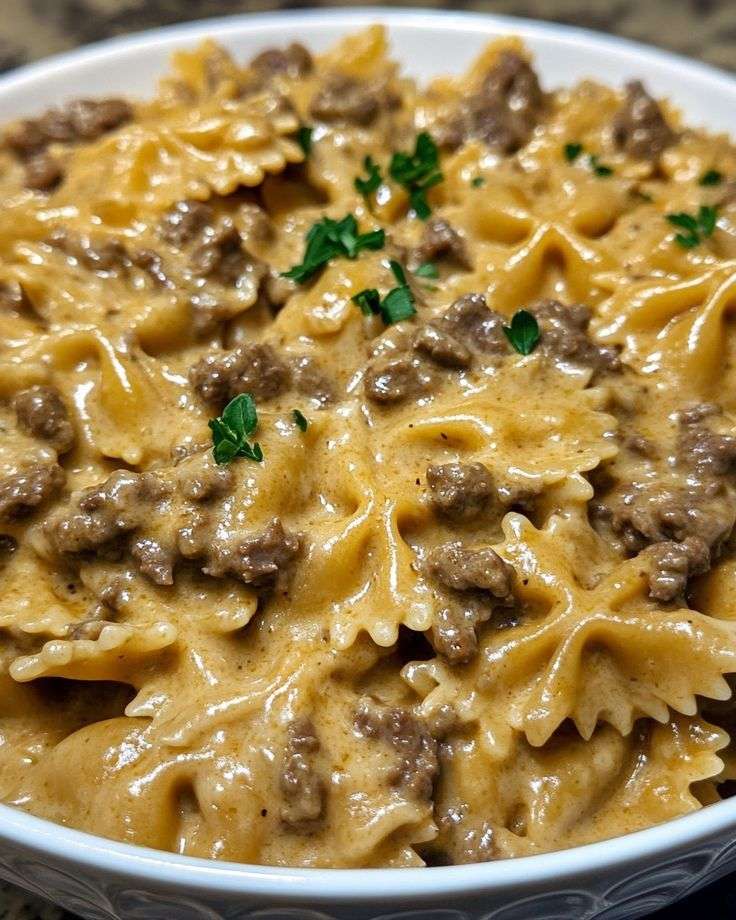 Assiette de pâtes papillon à la viande hachée, nappée de sauce crémeuse, parsemée de parmesan et de persil frais.