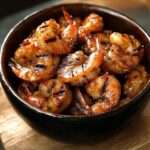 Crevettes sautées caramélisées au miel et épices, servies dans une assiette avec herbes fraîches.