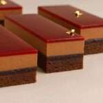 Entremet New York Chocolat Framboise en tranches, superposé de couches nettes, glaçage brillant et framboises fraîches.