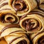 Crêpes garnies de Nutella et de fruits frais roulées et servies sur une assiette.