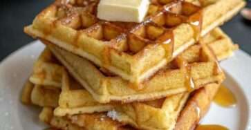 Assiette de gaufres dorées et croustillantes empilées, servies avec du beurre fondant et du sirop d’érable qui coule sur les carrés.