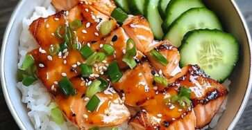 Bol de saumon teriyaki laqué servi sur du riz avec concombre frais, graines de sésame et ciboulette.