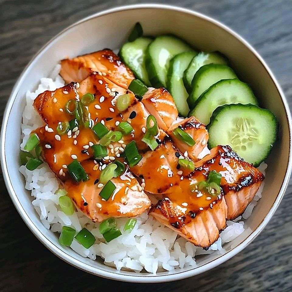 Bol de saumon teriyaki laqué servi sur du riz avec concombre frais, graines de sésame et ciboulette.