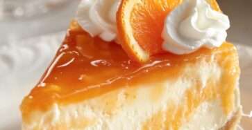 Cheesecake crémeux à l’orange avec base biscuitée et tranches d’orange fraîches sur le dessus.