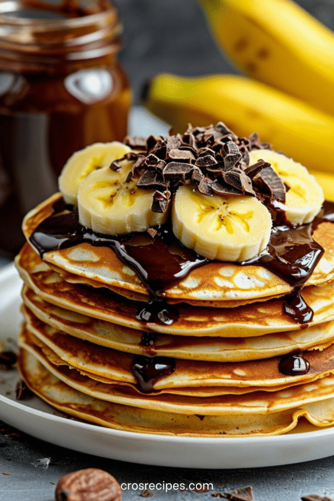 Empilement de pancakes banane chocolat moelleux, parsemés de pépites et garnis de banane fraîche.