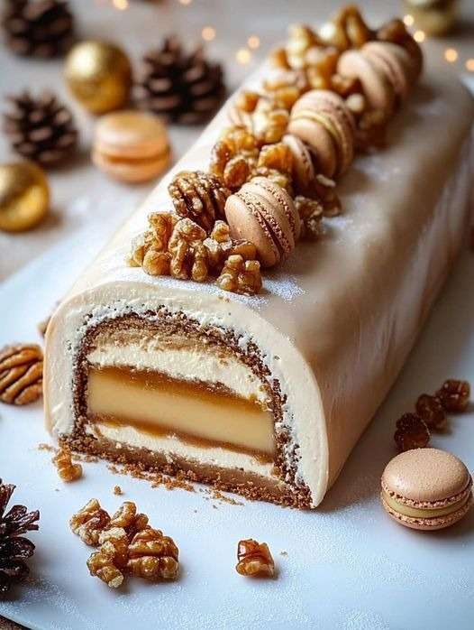 Bûche de Noël à la vanille, caramel et noisettes décorée de macarons et de noix sur un plateau festif.