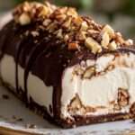 Bûche glacée vanille avec cœur praliné croustillant, nappée de chocolat noir craquant et décorée d’amandes torréfiées.