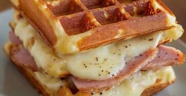 Assiette de gaufres salées dorées garnies de jambon et fromage fondant, servies en croque-gaufres croustillants avec salade verte sur le côté.