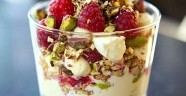 Verrines gourmandes à la crème mascarpone vanillée, framboises fraîches et pistaches concassées, présentées en couches colorées dans des verres transparents.