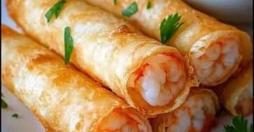 Cigares croustillants aux crevettes dorés, alignés sur une assiette avec herbes fraîches.