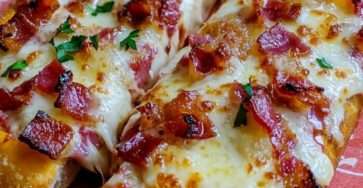 Pizza-baguette garnies de coulis de tomate, mozzarella fondue, lardons croustillants et persil frais servies sur une plaque de cuisson.