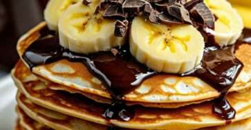 Empilement de pancakes banane chocolat moelleux, parsemés de pépites et garnis de banane fraîche.