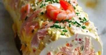 Bûche salée aux fruits de mer garnie de crabe, saumon fumé, gambas et zestes de citron sur un plat de service.