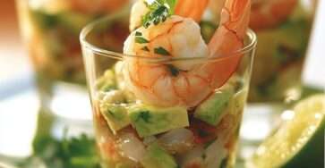 Verrines composées de couches d’avocat écrasé, tomates et crevettes, décorées d’herbes et de zeste de citron vert.