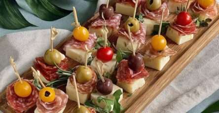 Mini brochettes apéritives composées de fromage, salami, olives et tomates cerises sur un plateau en bois.
