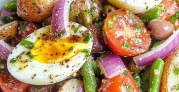 Salade tiède façon niçoise composée de pommes de terre fondantes, œufs mollets, tomates cerises, olives et haricots verts dans un grand saladier.