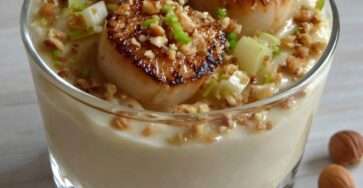 Verrines gastronomiques de Saint-Jacques poêlées posées sur une crème de panais, décorées de noisettes et oignon nouveau.