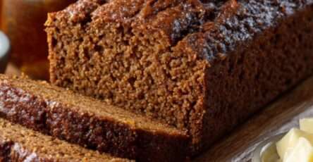 Pain d’épices moelleux parsemé d’amandes et de dés d’orange confite, tranché sur une planche en bois.